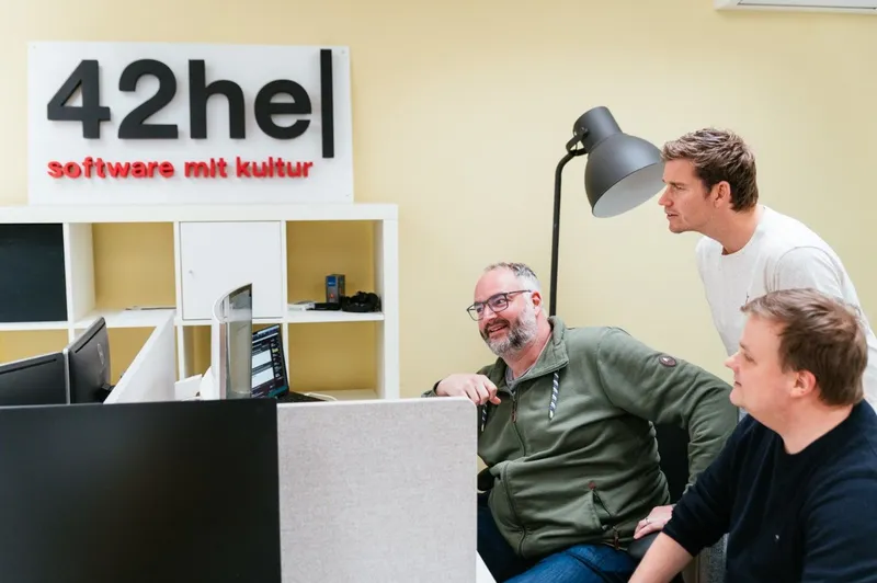 Arne, Axel und Christian betrachten Kundendaten. Im Hintergrund das 42he Logo.