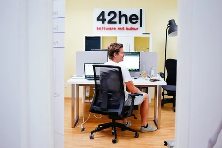 Axel, wie er im Büro am Computer sitzt, dahinter das 42he Logo.