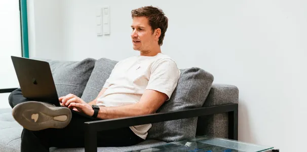 Axel sitzt auf der Couch und schreibt auf einem Laptop.