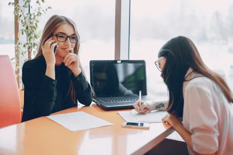 Zwei Frauen im Büro. Eine telefoniert, eine macht sich Aufzeichnungen.