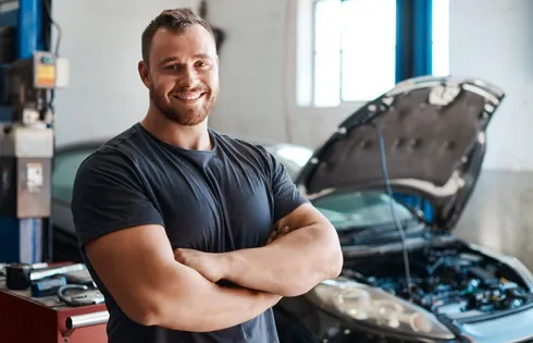 Handwerker posiert mit verschränkten Armen vor Motorhaube.
