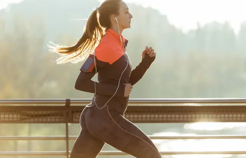 Eine Frau joggt vor malerischer Kulisse und hört dabei einen Podcast.