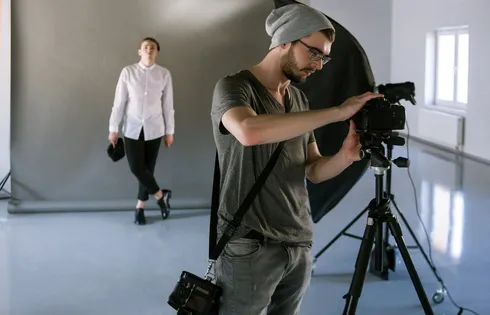 Ein Fotograf stellt seine Kamera ein, im Hintergrund ein Model.