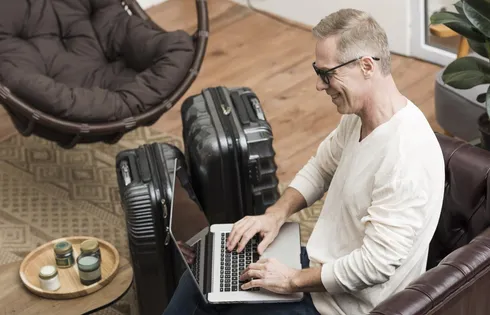 Mann sitzt lächelnd am Laptop in Hotelumgebung.