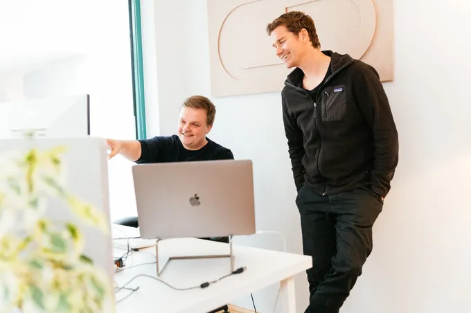 Christian und Axel im Büro vor einem Bildschirm. Christian zeigt auf den Bildschirm.