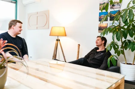 Axel und Christian sehen sich an, im Hintergrund leuchtet eine Stehlampe.